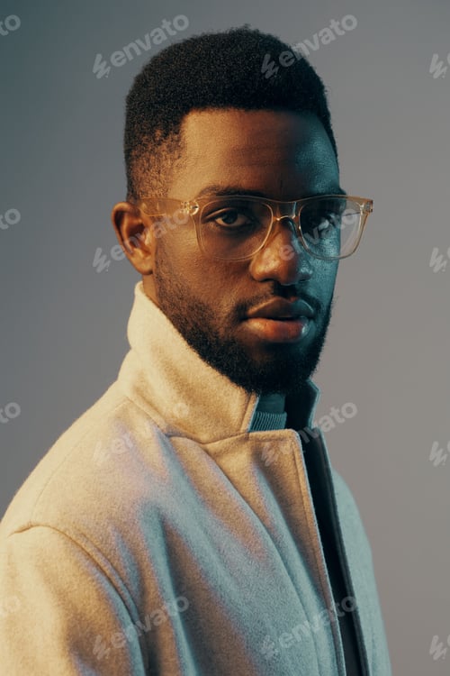 Preview: Stylish young Black man with glasses in a soft pastel background, showcasing modern fashion and