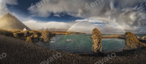 Preview: Panoramic view of sea with rocks and rainbow under cloudy sky in Iceland