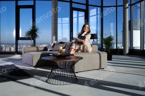 Preview: Attractive woman holding book while relaxing on couch
