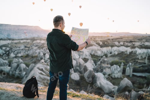 Preview: Unrecognizable traveler looking at detailed map of terrain and air balloons over highlands