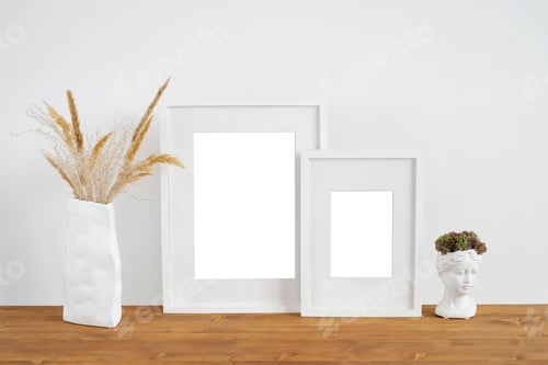 Preview: Mockup of two white photo frames on a wooden table with a vase of dried flowers and a plaster bust.