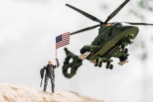 Preview: toy soldier holding american flag while standing on sand near helicopter