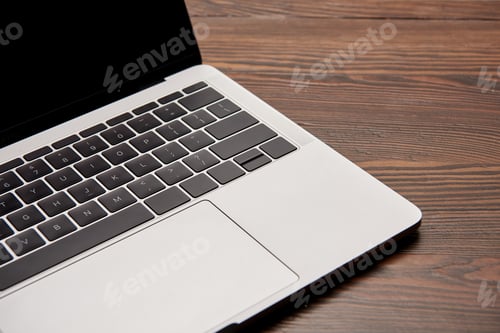 Preview: partial view of laptop with blank screen on wooden table