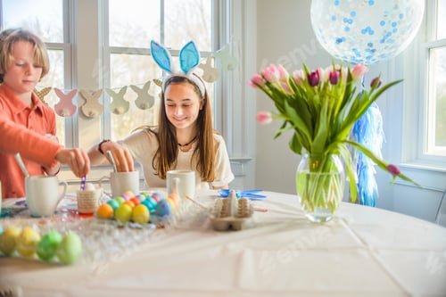 Preview: Teenage girl and brother dyeing hard boiled eggs for Easter at table