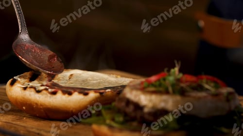 Preview: Male chef hands preparing burger in dark room and adding liquid red wine sauce on a toasted burger