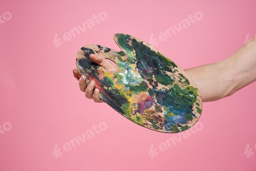 Preview: Artist's hand paints palette easel for drawing training pink background