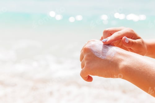 Preview: Woman in swimwear is applying sun cream on her hand with her finger at the sea background