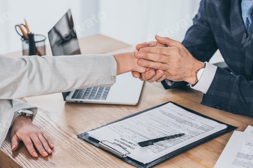 Preview: cropped view of businessman holding woman hand over table in office, compensation concept