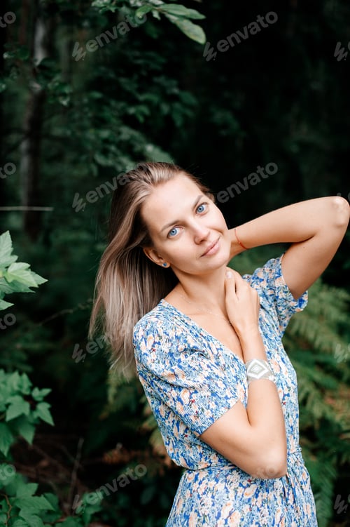 Preview: A girl in a blue dress stands in a green forest and holds her neck with her hands