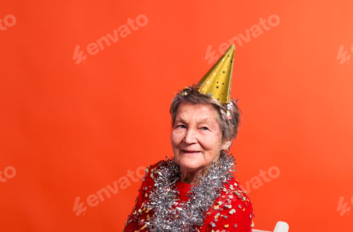 Preview: Portrait of a senior woman in studio on a red background. Party concept.