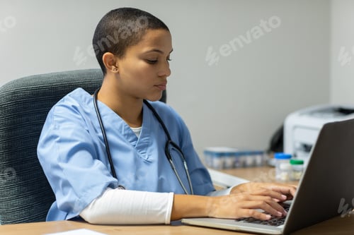 Preview: Front view of mixed-race female doctor working on laptop at desk of examination room in hospital