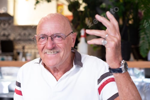 Preview: Portrait of happy smiling bald head senior man sitting at cafe table looking at camera talking