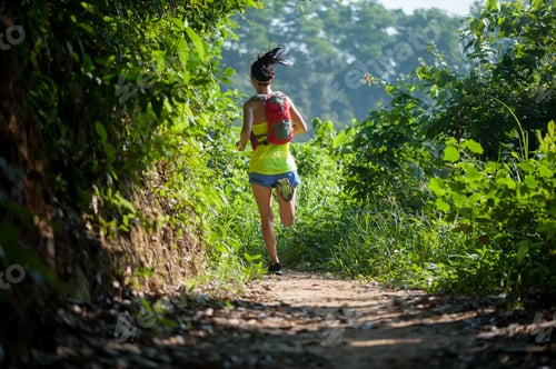 Preview: Young woman trail runner running in sunrise tropical forest