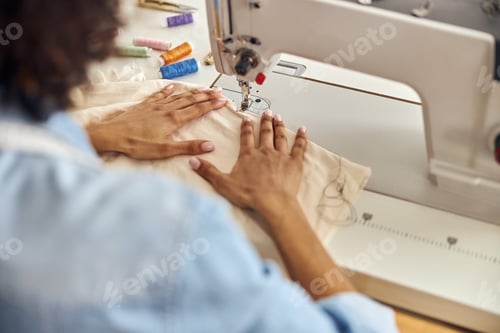 Preview: African-American worker sews white fabric with machine tool at table in studio