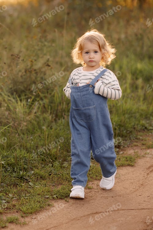 Preview: A young blonde girl in a blue jumpsuit walks along a dirt road in the park