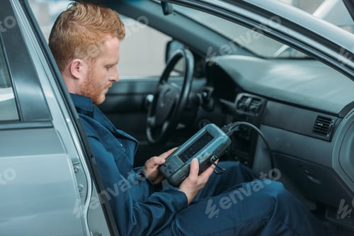 Preview: Automechanic sitting in a car, using a car diagnostic tool