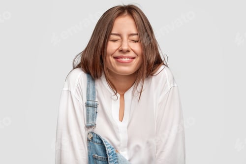 Preview: Happy overjoyed young female smiles positively, closes eyes with pleasure, laughs at good joke, has