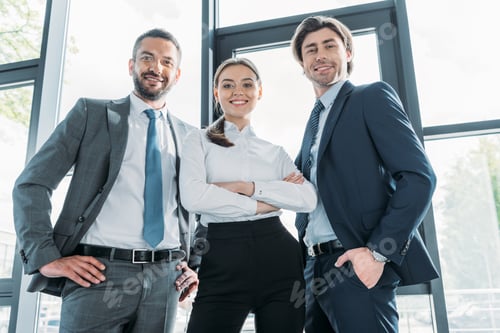 Preview: bottom view of group of smiling young business people standing at modern office and looking at