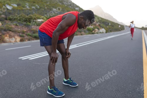 Preview: Fit african american man in sportswear standing and resting on a coastal road