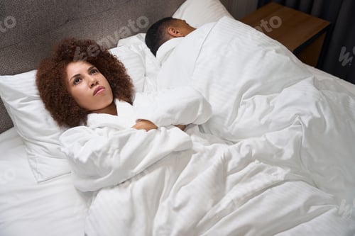 Preview: Upset multiracial woman lying on bed in hotel room