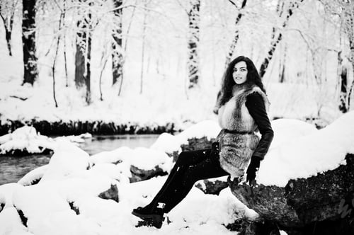 Preview: Elegance curly girl in fur coat at snowy forest park at winter.