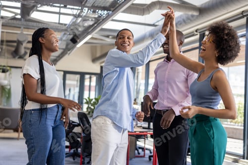 Preview: Colleagues celebrating success with high fives and laughter in modern office