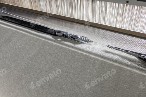 Preview: High-speed loom shuttle weaving fabric, detail of warp threads and industrial textile machinery.