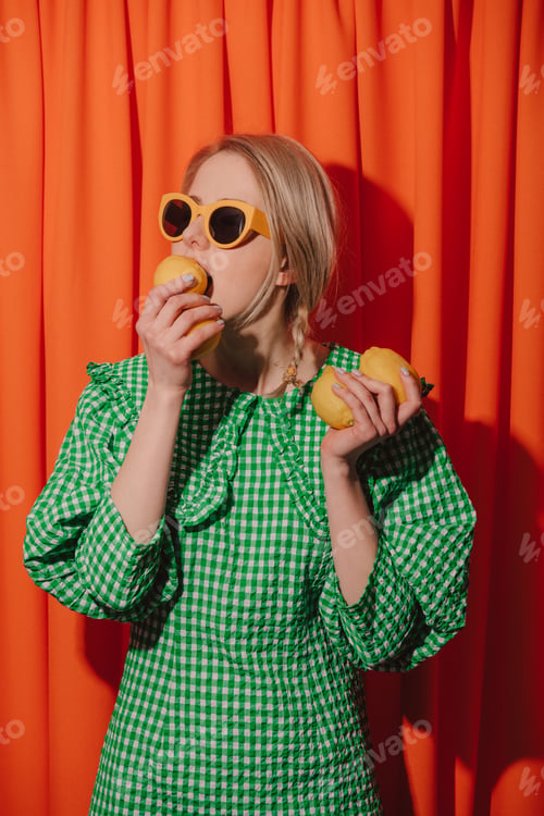 Preview: Style woman in green dress and sunglasses with lemons on orange curtains background