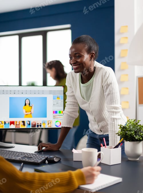 Preview: Satisfied african photo editor discussing with colleague how retouching image