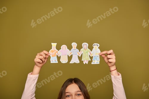 Preview: Cropped view of preteen girl holding hand-drawn paper characters above head and looking at camera