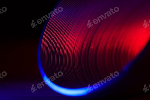 Preview: Closeup of coiled metal spring with sufficiently high strength in red blue neon light. Macro shot.