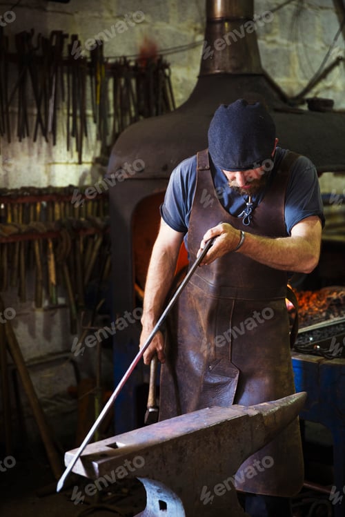 Preview: A blacksmith in a leather apron holds a thin length of metal against an anvil in a workshop.