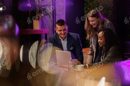 Preview: Cheerful work colleagues working on a laptop while having a meeting in a cafe