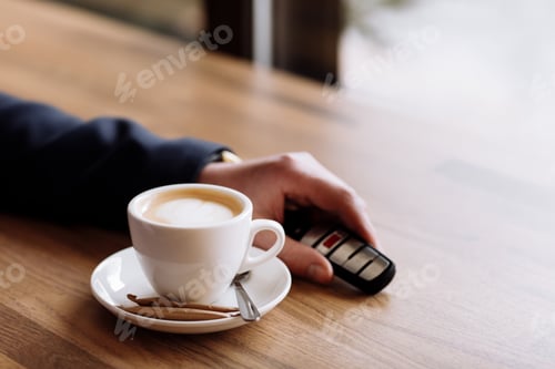 Preview: Close view of car keys put on the table next to cup of coffee by rich suited businessman in the cafe