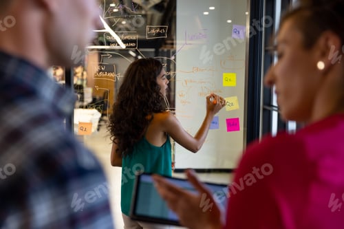 Preview: Diverse male and female colleagues brainstorming using tablet and making notes on glass wall