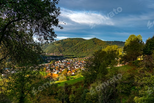 Preview: Scenic town nestled in green hills under a cloudy sky.