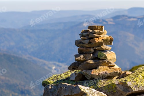 Preview: Stack of stones covered with moss on top of a mountain on mountains background.