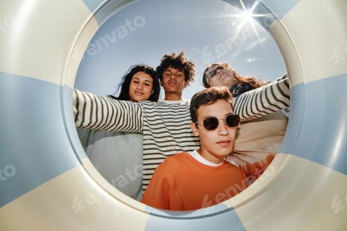 Preview: Four Teenagers Posing Together Holding Swimming Tube in Sunshine on Beach