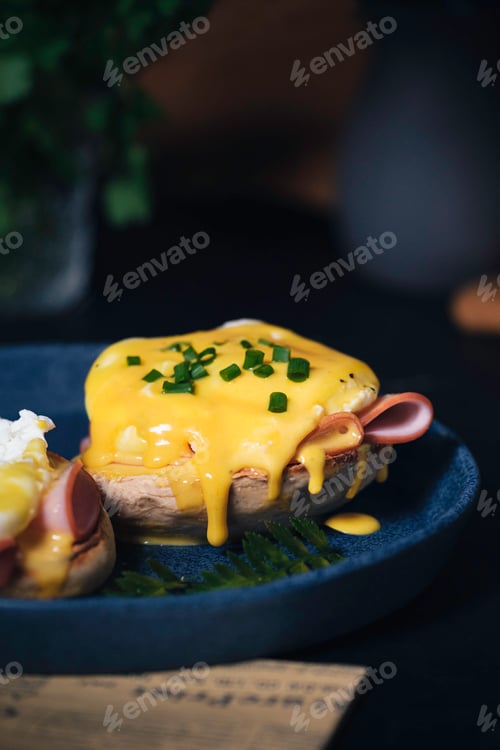 Preview: egg Benedict with hollandaise sauce on dark blue plate on table in kitchen