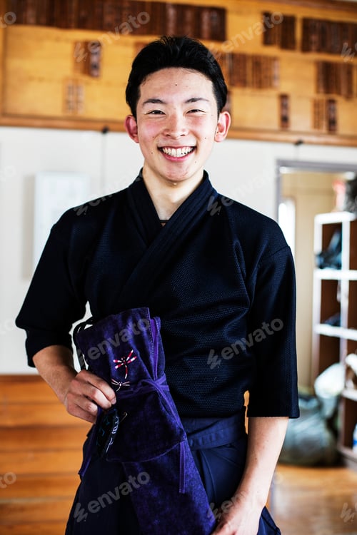 Preview: Male Japanese Kendo fighter standing in a gym, smiling at camera.