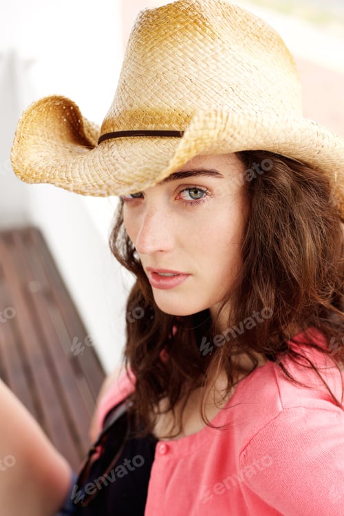 Preview: Serious young lady sitting outside wearing hat
