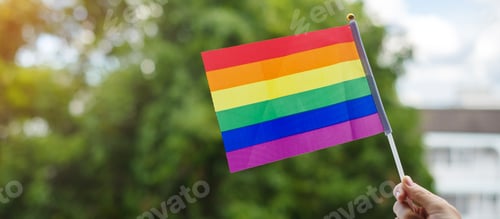 Preview: hands showing LGBTQ Rainbow flag on green nature background. Pride month concept