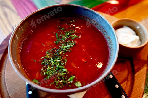 Preview: Delicious bowl of red soup garnished with herbs served with a side of cream in a vibrant restaurant