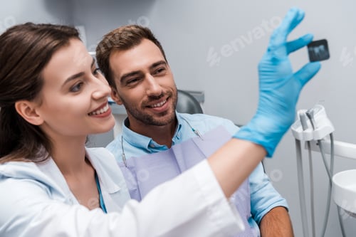 Preview: selective focus of attractive dentist and smiling patient looking at x-ray