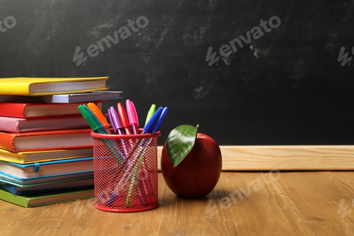 Preview: Different stationery and red apple on wooden table near blackboard, space for text