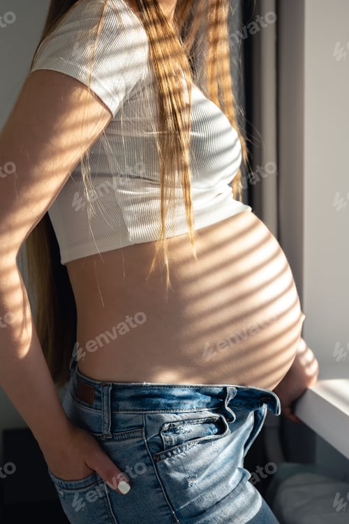 Preview: A pregnant woman at the window on a sunny morning.