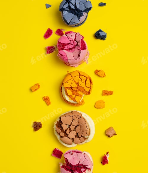 Preview: broken round macarons with crumbs on a yellow background, delicious dessert, top view