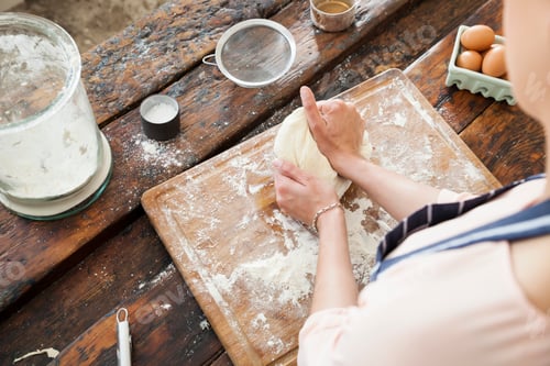 Preview: Over shoulder view of young woman kneading dough on chopping board