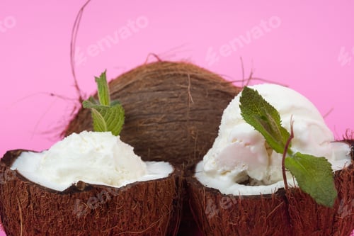 Preview: Vanilla ice cream balls in fresh coconut halves decorated with mint leaves on a pink background