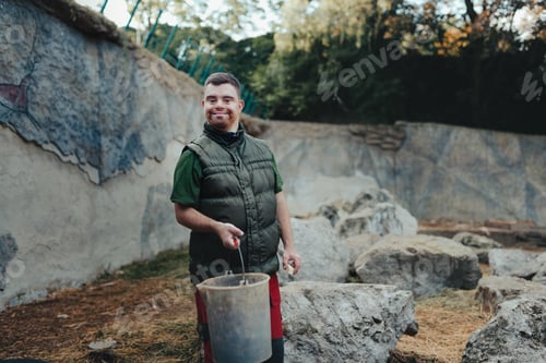 Preview: Caretaker with down syndrome in zoo giving food in animal enclosure. Concept of integration people